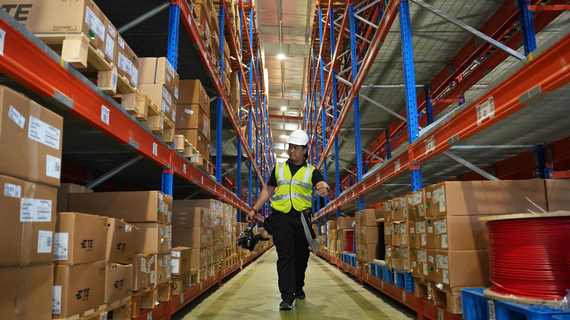 Man in reflective vest walks down warehouse aisle.