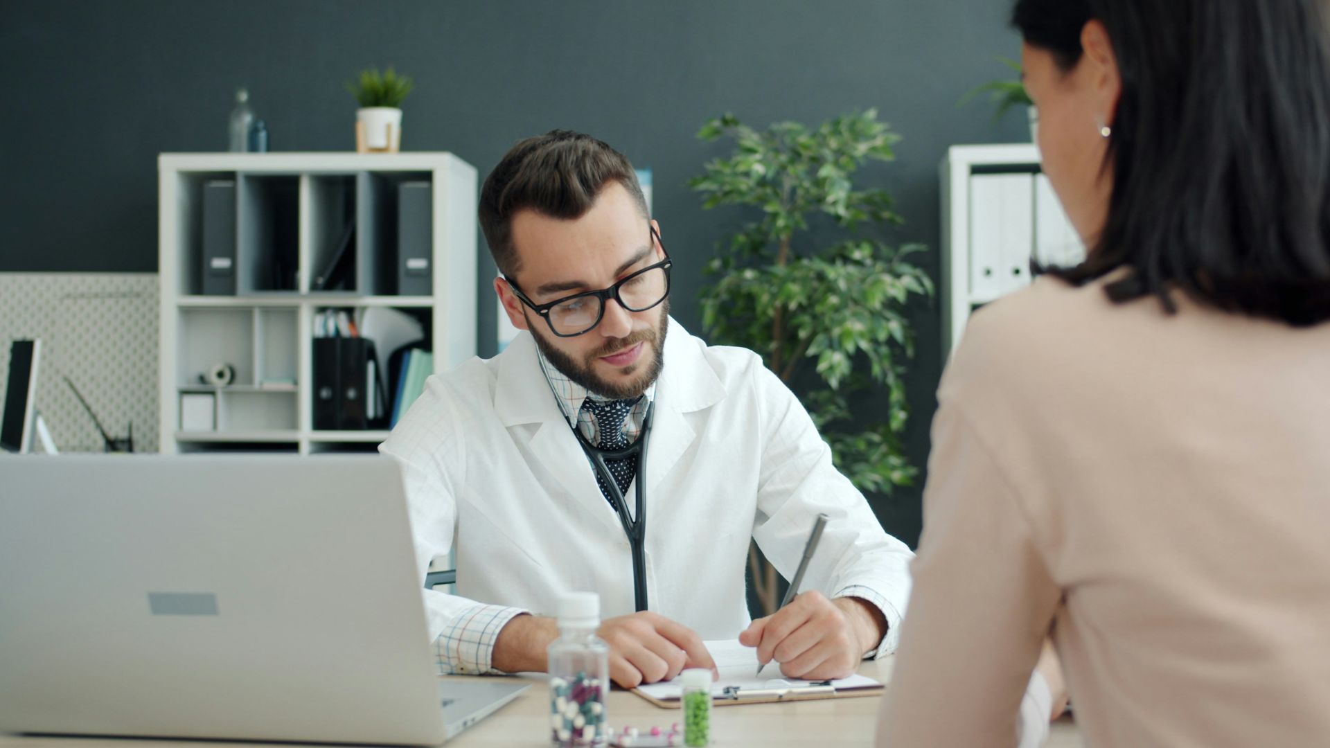 Doctor writing notes while patient sits opposite.