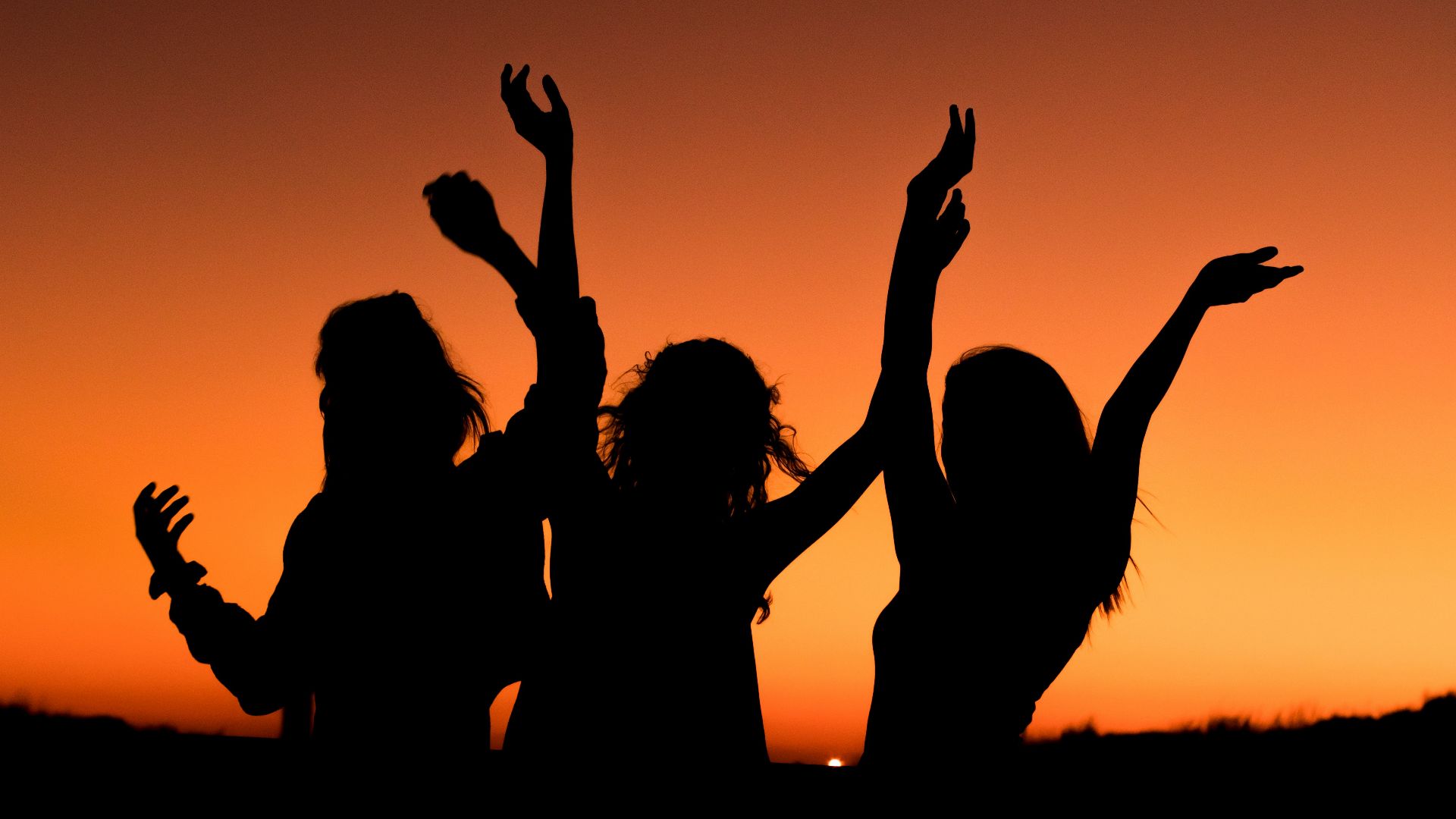 silhouette of three woman with hands on the air while dancing during sunset