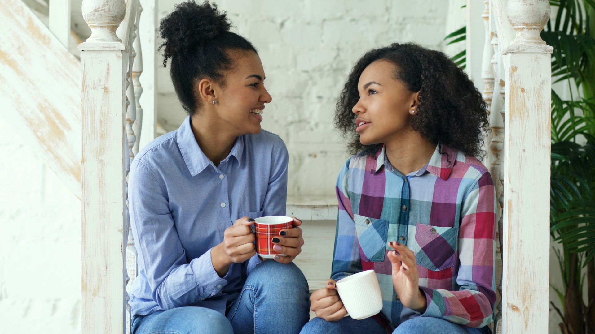 Two women talking while holding coffee mugs on stairs.
