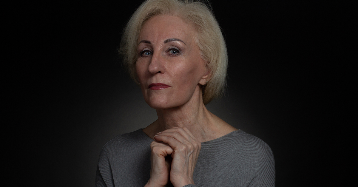 Classic portrait of an elderly blonde woman in Studio on black background. hands folded on rude, the concept of supplication, uncertainty