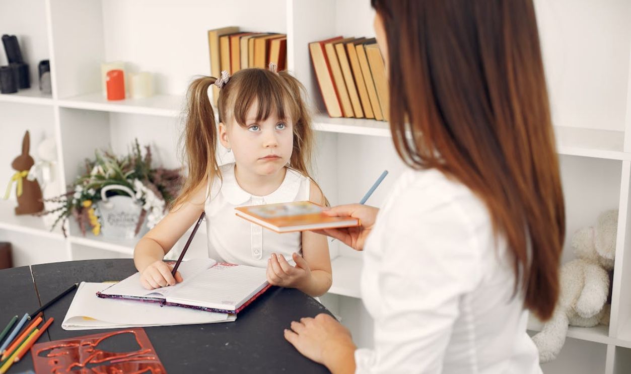Cute schoolchild doing homework with help of tutor