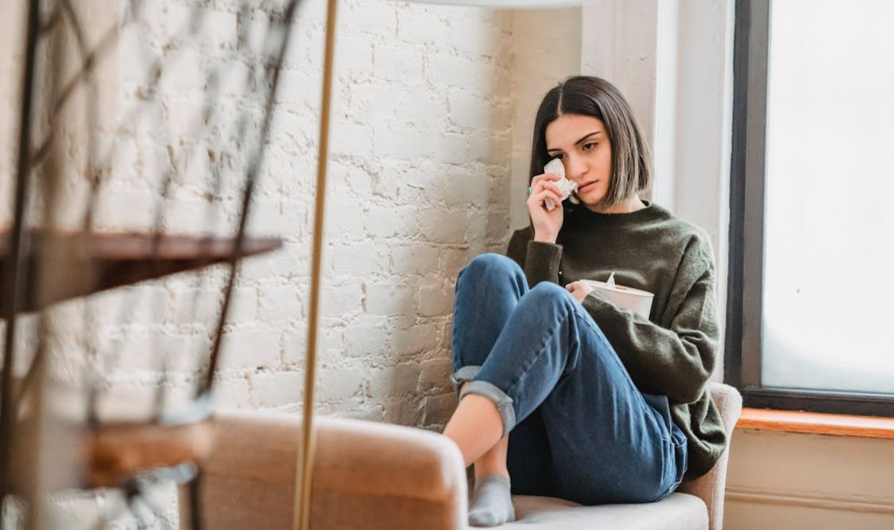 Desperate young ethnic female millennial crying on couch and wiping tears
