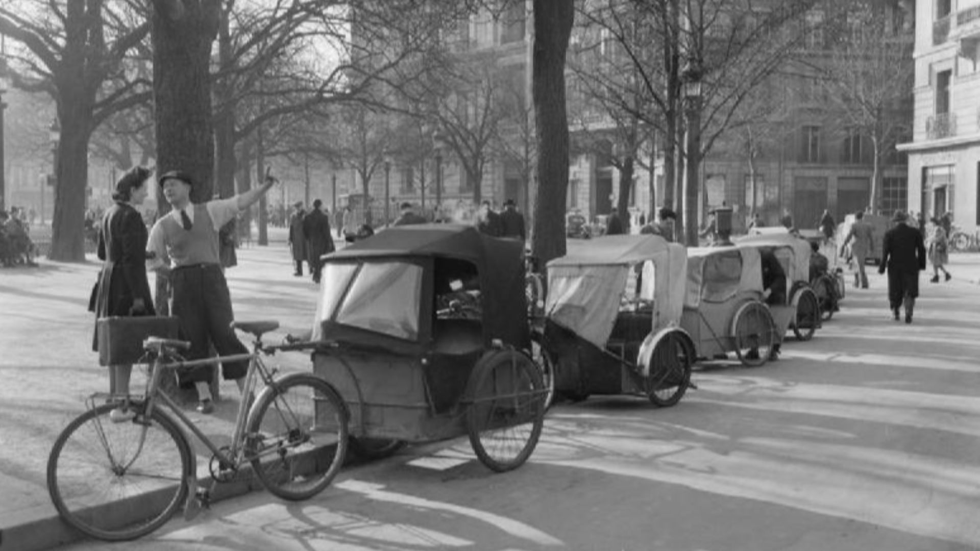 Parisian Traffic, Spring 1945- Everyday Life in Paris, France, 1945
A general view of a cab rank: French style!  A row of Velo taxis line the kerb of a leafy street in the Spring sunshine, somewhere in Paris.  Pedestrians can be clearly seen, going about their daily business.