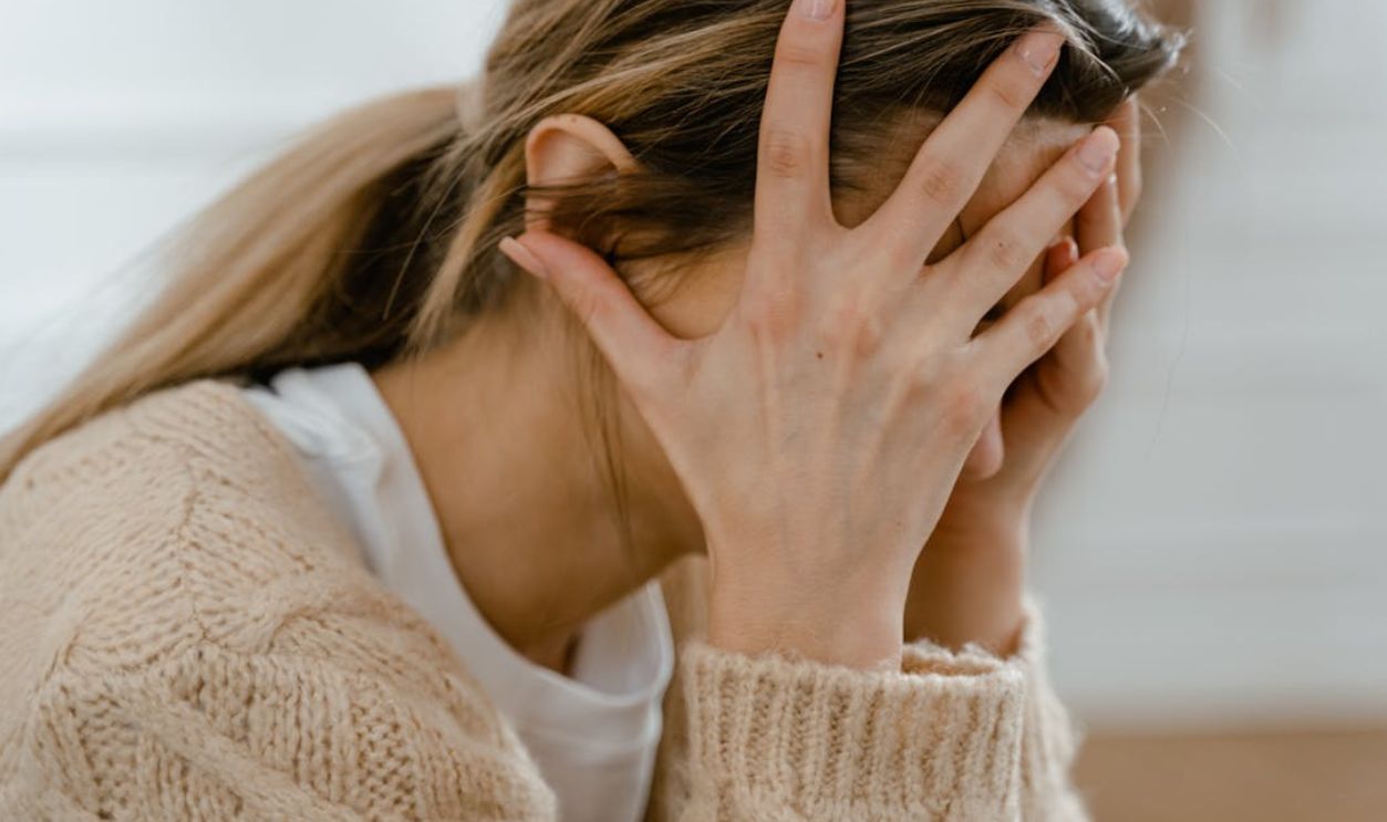 Woman sitting indoors with face covered by hands, expressing stress and frustration