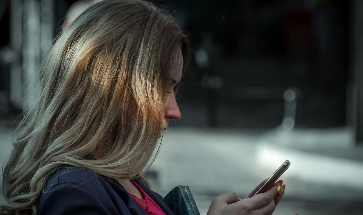 Side profile of a young woman texting on her smartphone in a shaded outdoor area