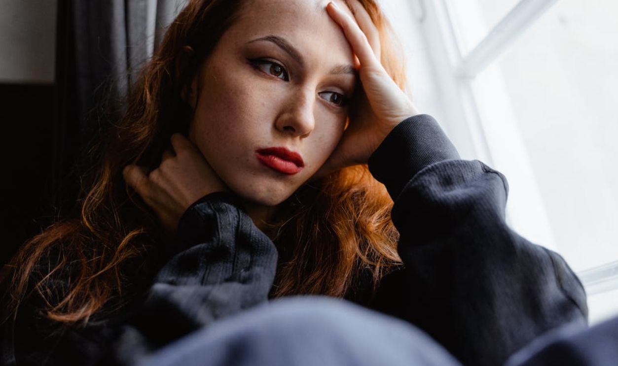 A young woman with a thoughtful expression gazes out the window in a moment of introspection