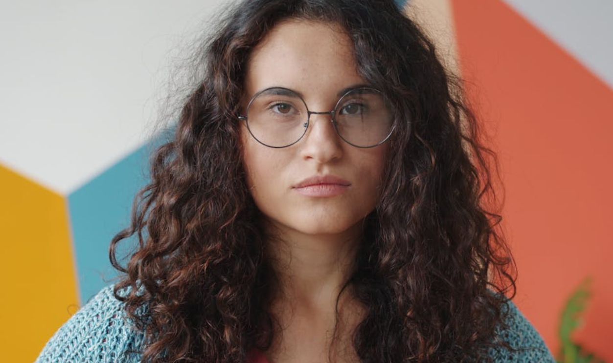 Confident woman with curly hair and glasses against a geometric background. Colorful and modern