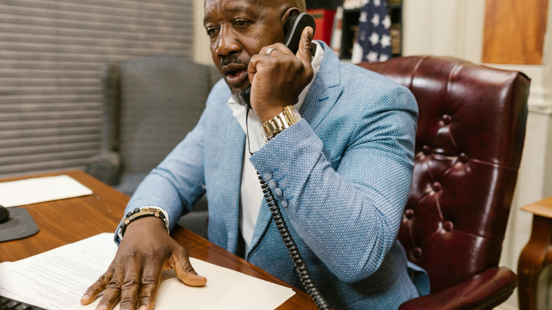 African American man in a blue suit speaking on the phone in a professional office setting