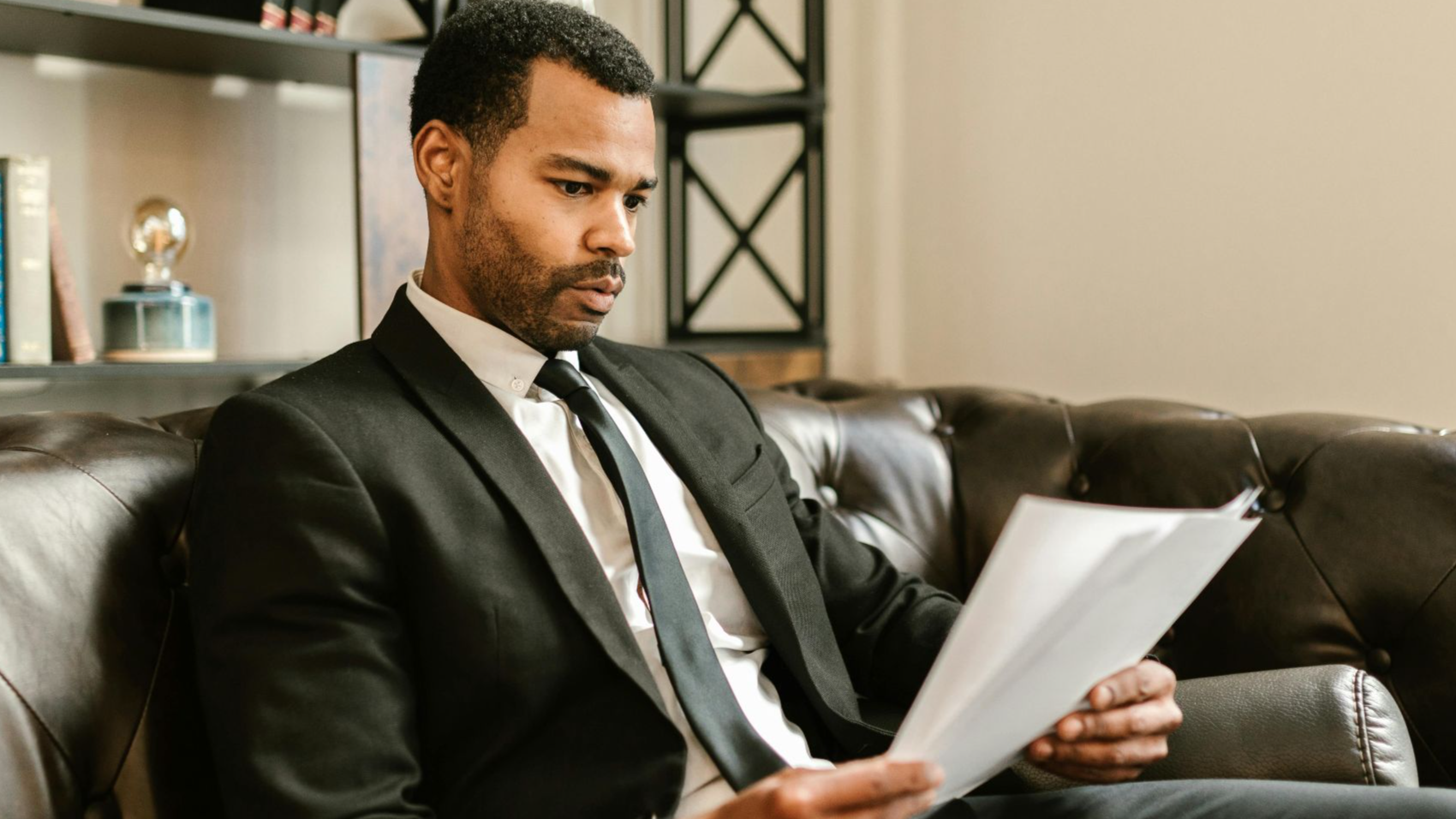 Businessman in suit reading papers on a leather sofa in a modern office setting