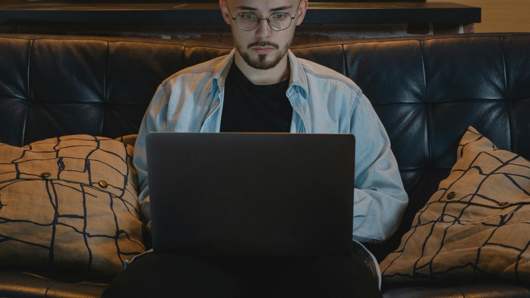 Man working remotely on a laptop in a cozy, stylish apartment with exposed brick walls and modern decor.