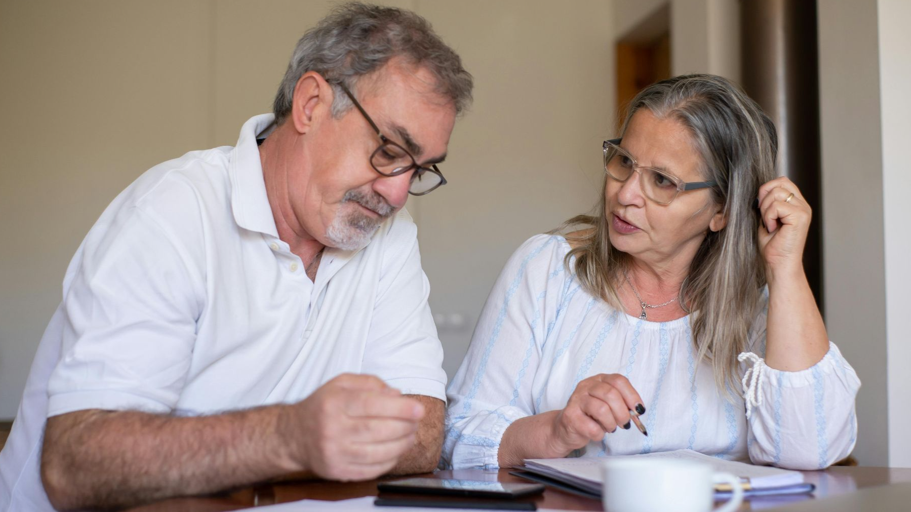Senior couple reviewing documents and managing finances together at home, showing collaboration and care.