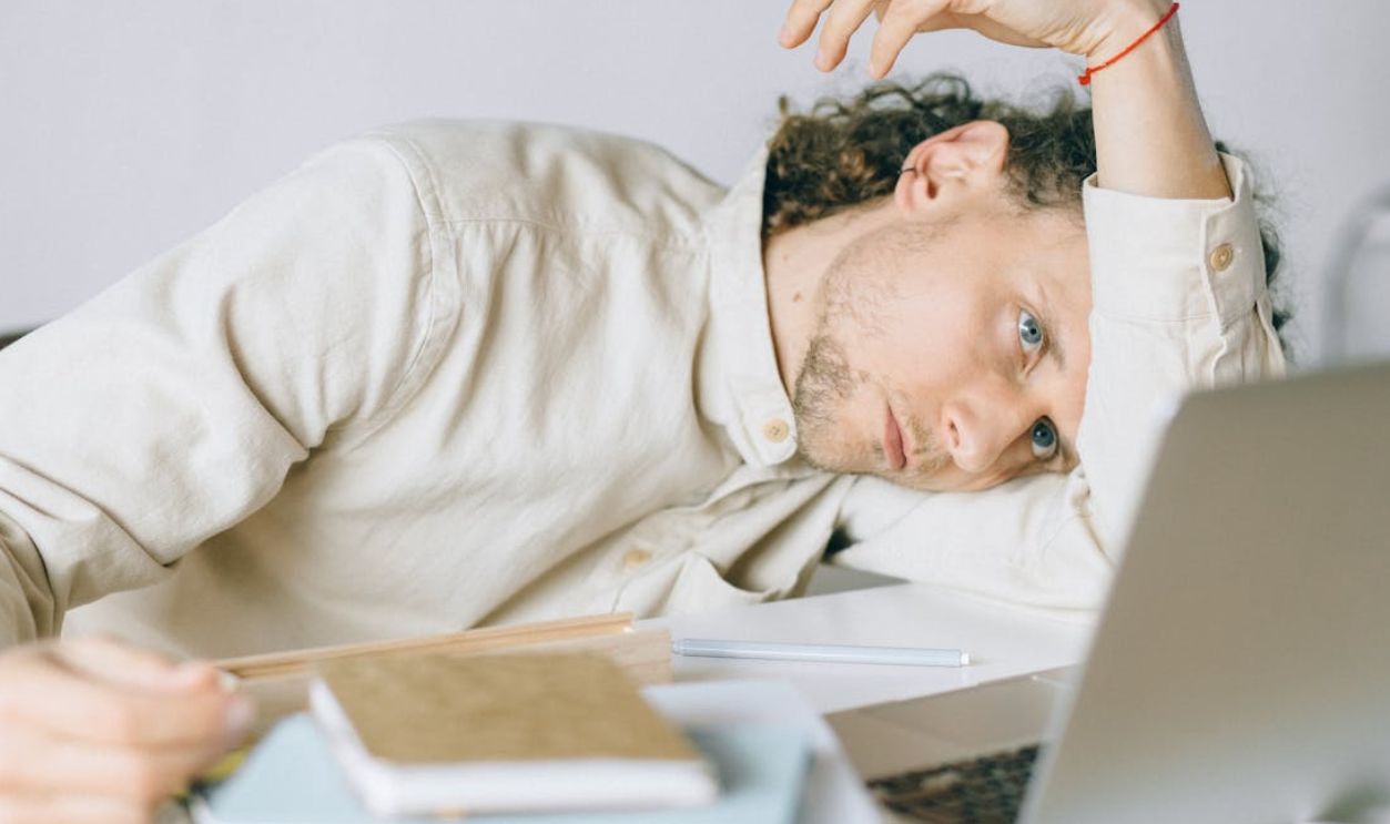 A tired Caucasian man at a desk, showing signs of exhaustion and stress, exemplifying workplace burnout