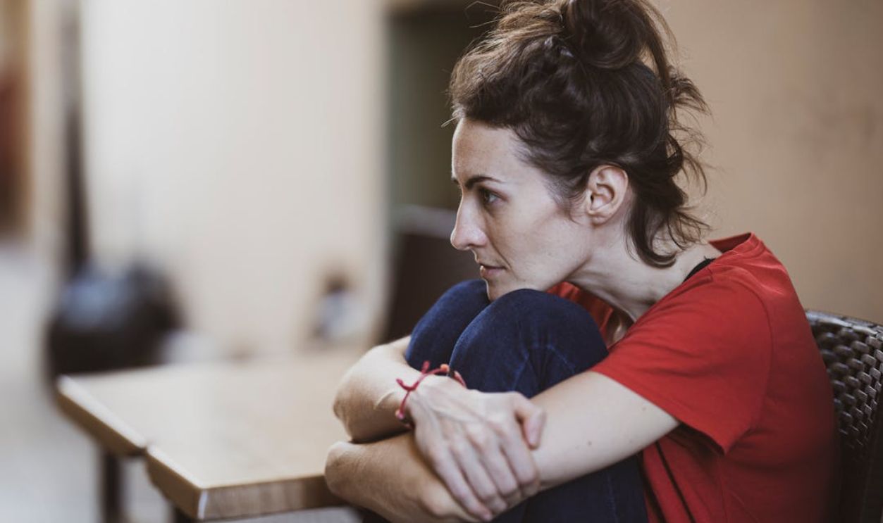 A contemplative woman in casual clothes sits indoors, deep in thought