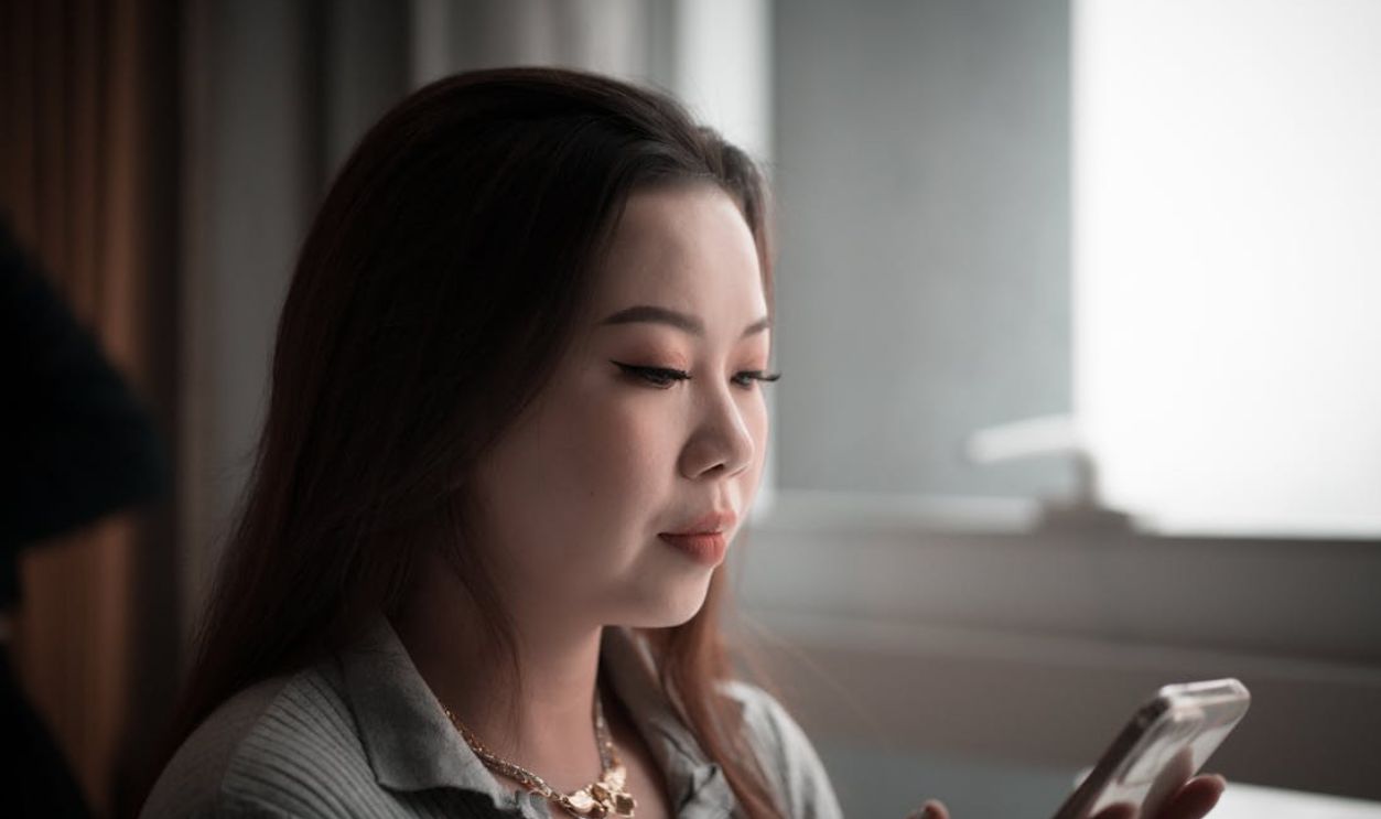 Young Asian woman using smartphone indoors, focused on screen