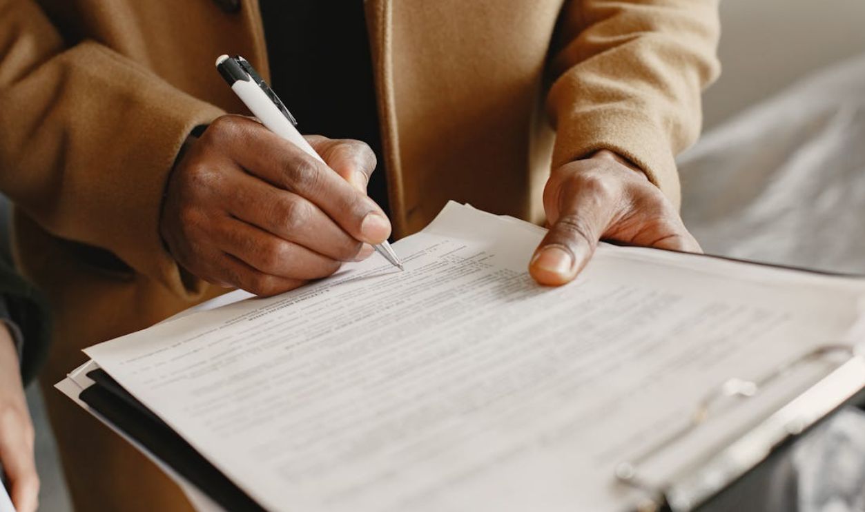 Close-up of a person signing a contract on a clipboard, focusing on legal formalities