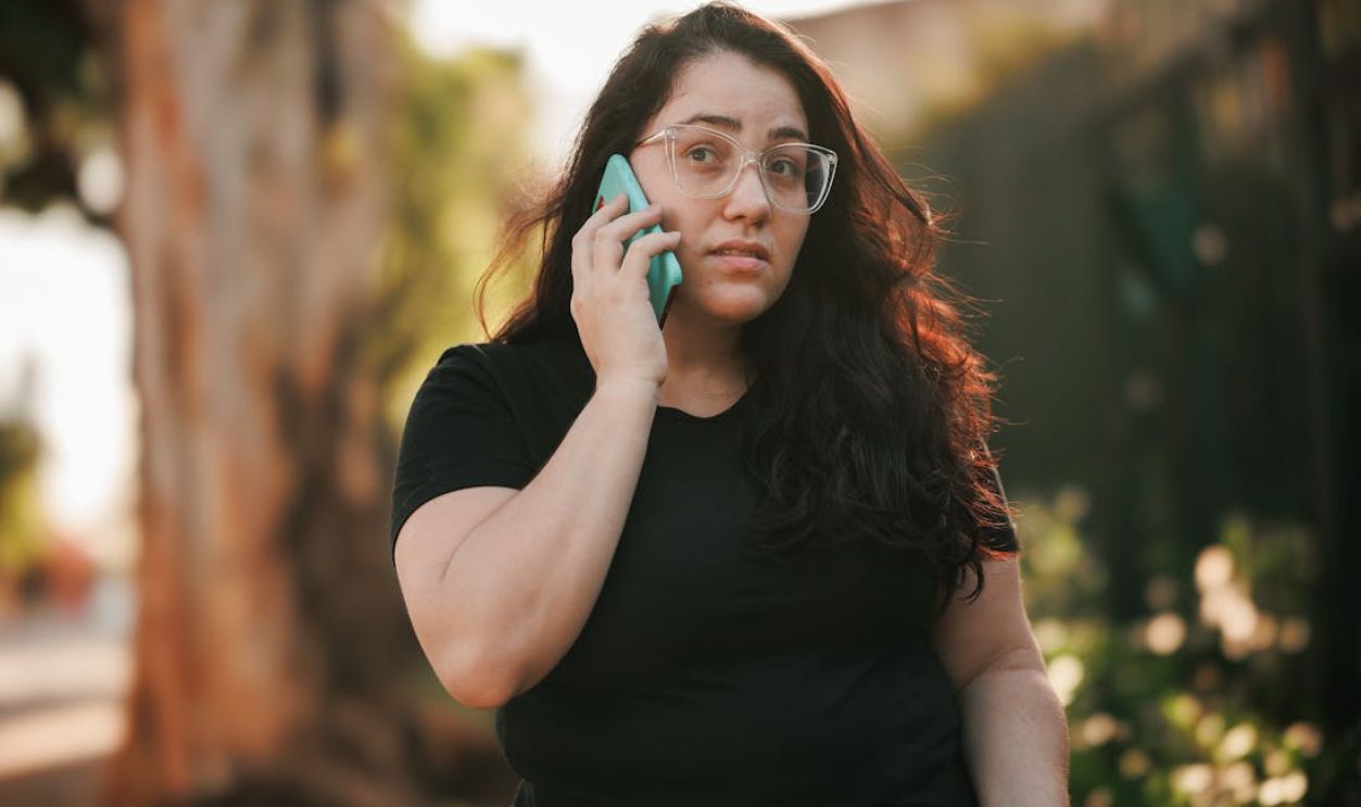 Woman with eyeglasses talks on smartphone in sunny park setting