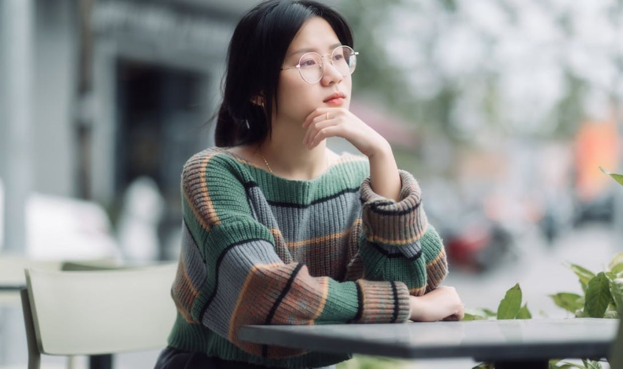 Woman in glasses ponders at an outdoor cafe, wearing a striped sweater