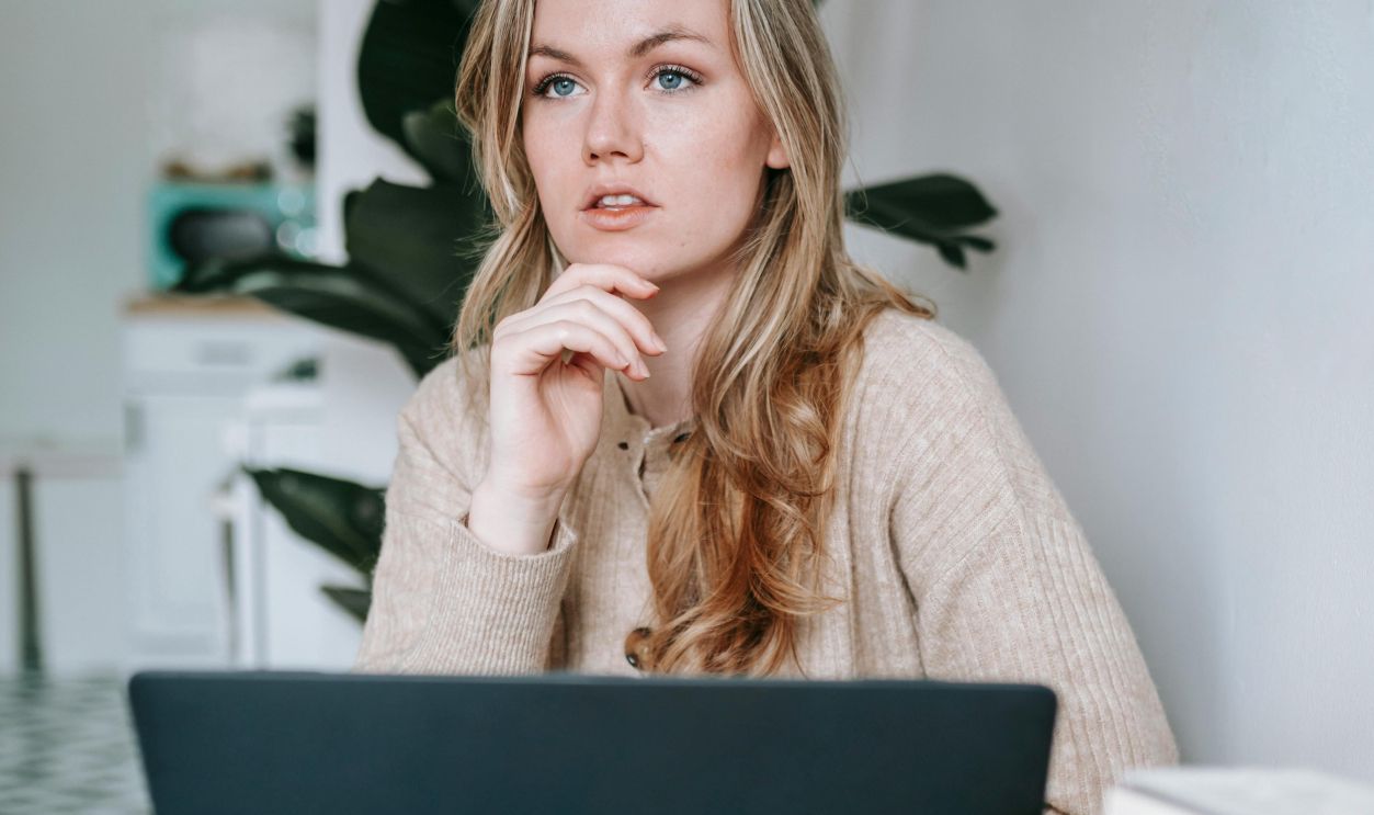 A woman pondering over work at home, surrounded by books and using a laptop