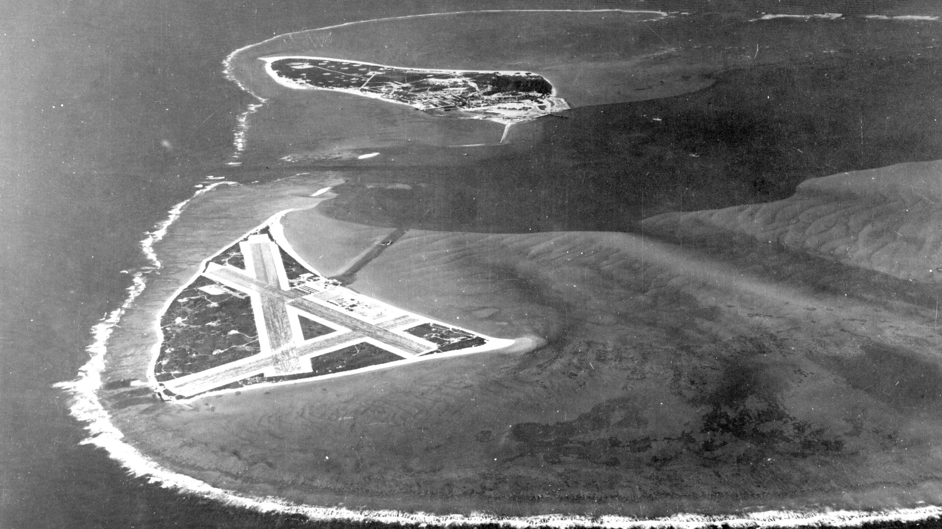 Aerial photograph of Midway Atoll, looking just south of west across the southern side of the atoll, 24 November 1941. Eastern Island, then the site of Midway's airfield, is in the foreground. Sand Island, location of most other base facilities, is across the entrance channel.