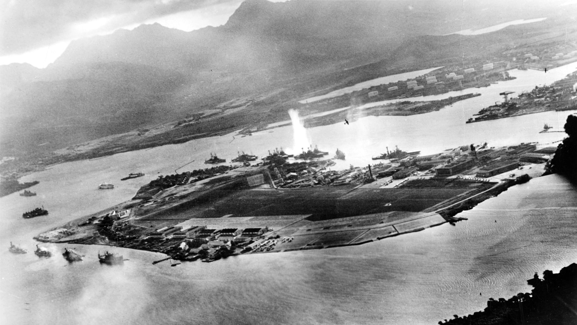 Photograph taken from a Japanese plane during the torpedo attack on ships moored on both sides of Ford Island shortly after the beginning of the Pearl Harbor attack. View looks about east, with the supply depot, submarine base and fuel tank farm in the right center distance.
A torpedo has just hit USS West Virginia on the far side of Ford Island (center). Other battleships moored nearby are (from left): Nevada, Arizona, Tennessee (inboard of West Virginia), Oklahoma (torpedoed and listing) alongside Maryland, and California.
On the near side of Ford Island, to the left, are light cruisers Detroit and Raleigh, target and training ship Utah and seaplane tender Tangier. Raleigh and Utah have been torpedoed, and Utah is listing sharply to port.

Japanese planes are visible in the right center (over Ford Island) and over the Navy Yard at right. U.S. Navy planes on the seaplane ramp are on fire.