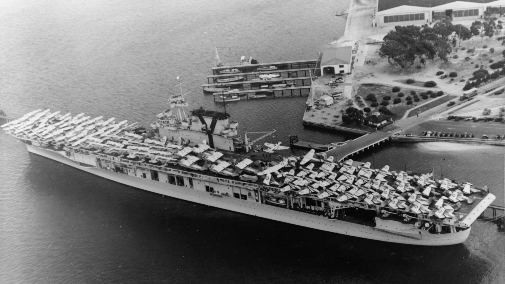 The U.S. Navy aircraft carrier USS Yorktown (CV-5) at Naval Air Station North Island, San Diego, California (USA), in June 1940, embarking aircraft and vehicles prior to sailing for Hawaii. Aircraft types on her flight deck include Douglas TBD-1 Devastator, Northrop BT-1, Curtiss SBC-3 Helldiver, Grumman F3F-2, Grumman F3F-3, Vought SB2U Vindicator, Grumman JRF, Grumman J2F Duck and Sikorsky JRS-1. Some of these planes were on board for transportation, while others were members of the ship's air group. Three Torpedo Squadron 5 (VT-5) TBDs at the after end of the flight deck are painted in experimental camouflage schemes tested during exercise