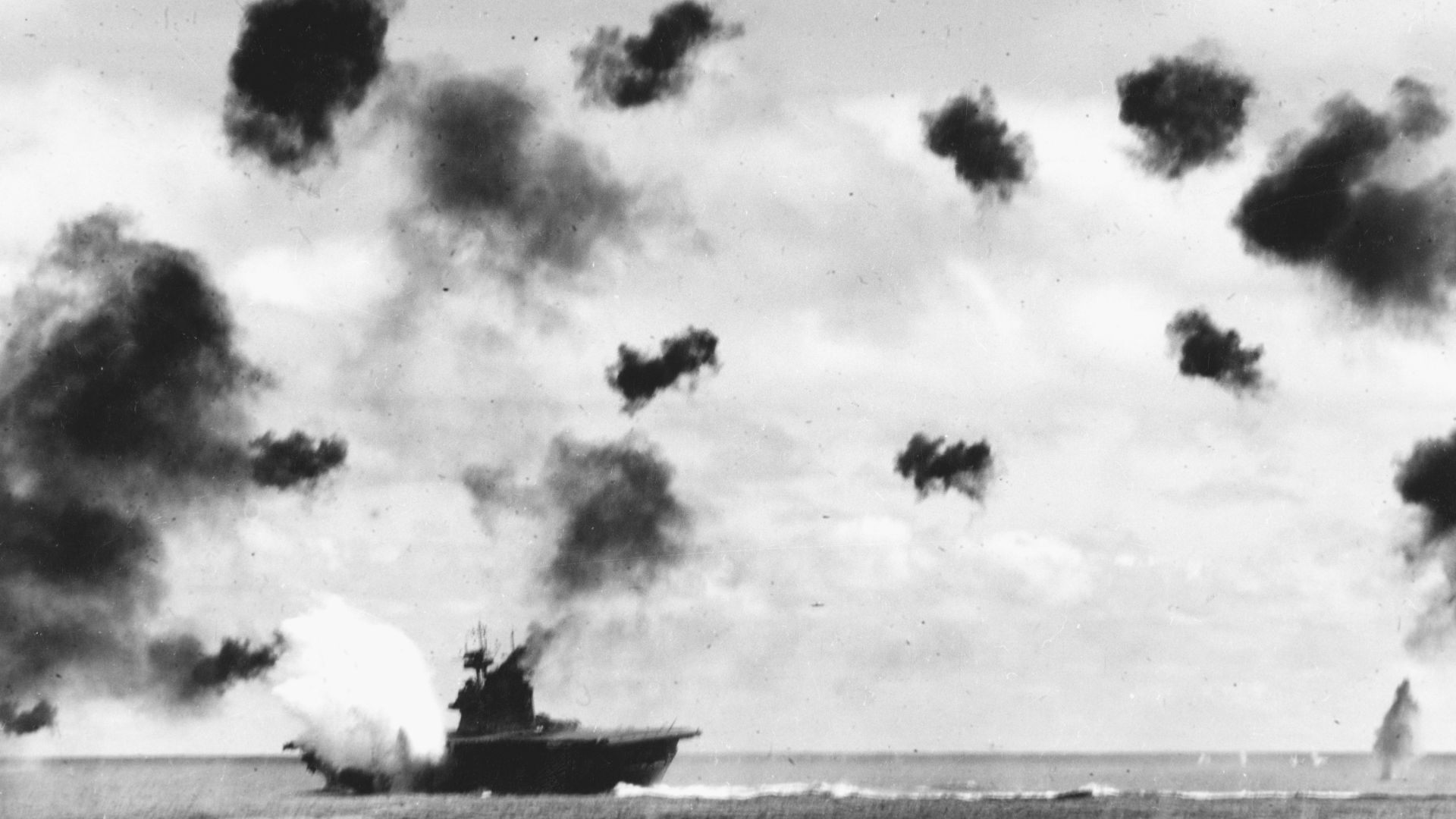 USS Yorktown (CV-5) is hit on the port side, amidships, by a Japanese Type 91 aerial torpedo during the mid-afternoon attack by planes from the carrier Hiryu, in the Battle of Midway, on 4 June, 1942. Yorktown is heeling to port and is seen at a different aspect than in other views taken by USS Pensacola (CA-24), indicating that this is the second of the two torpedo hits she received. Note very heavy anti-aircraft fire.