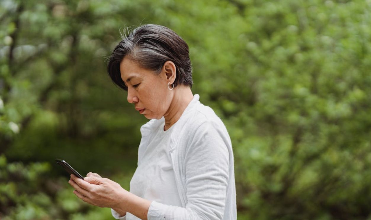 Woman checking phone amidst lush greenery. Perfect for lifestyle or technology themes