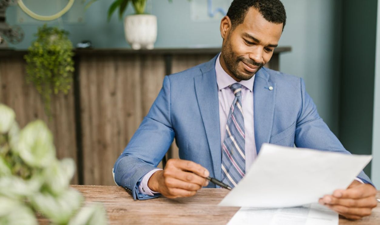 Smiling businessman in blue suit reviewing documents at a wooden table in modern office setting
