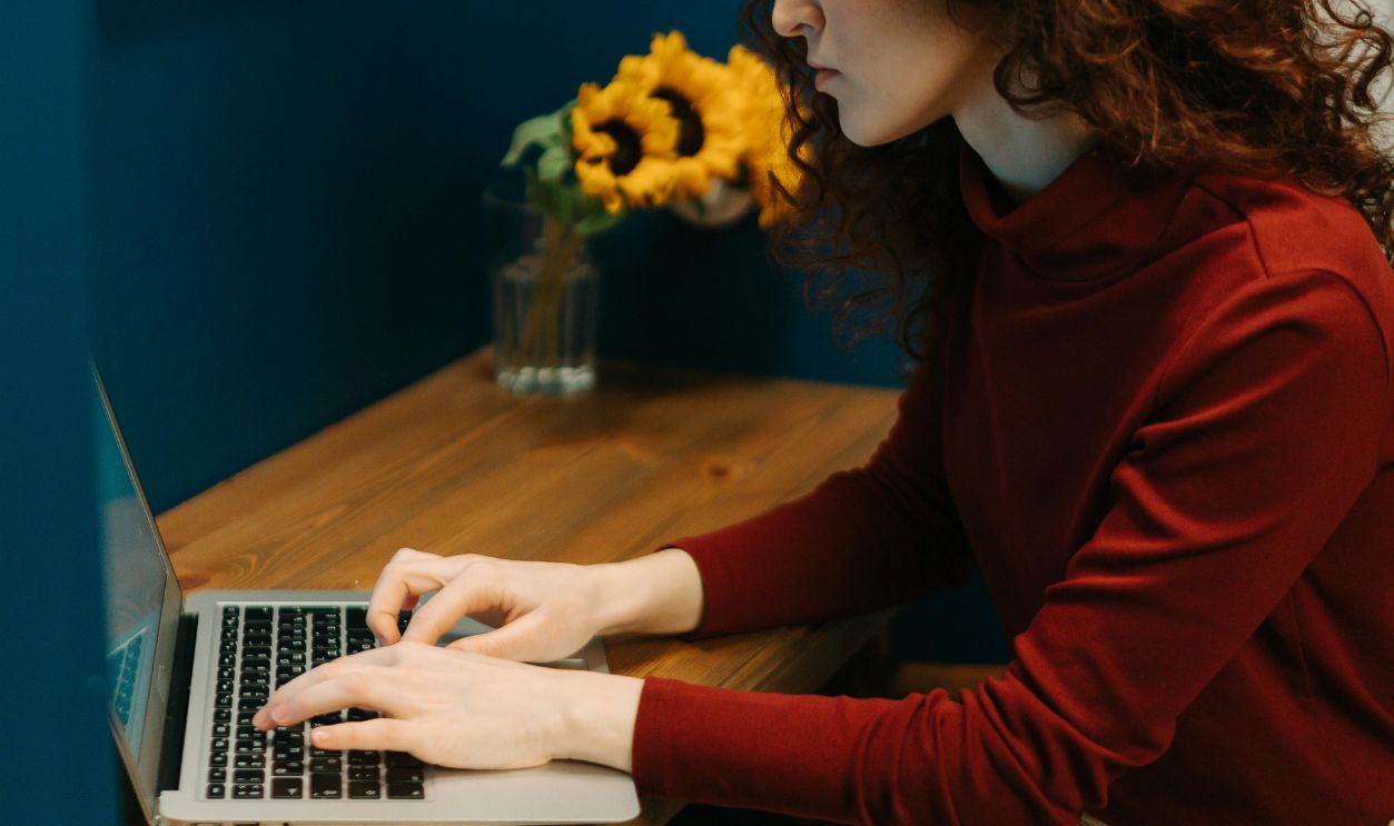 Redhead woman typing on a laptop in a cozy home office with blue walls