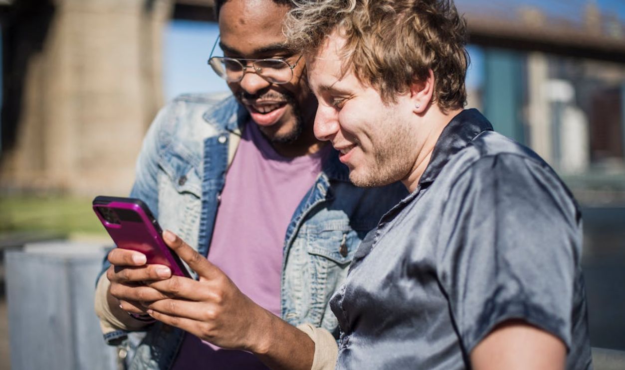 Smiling interracial gay couple joyfully looking at smartphone in sunny urban setting