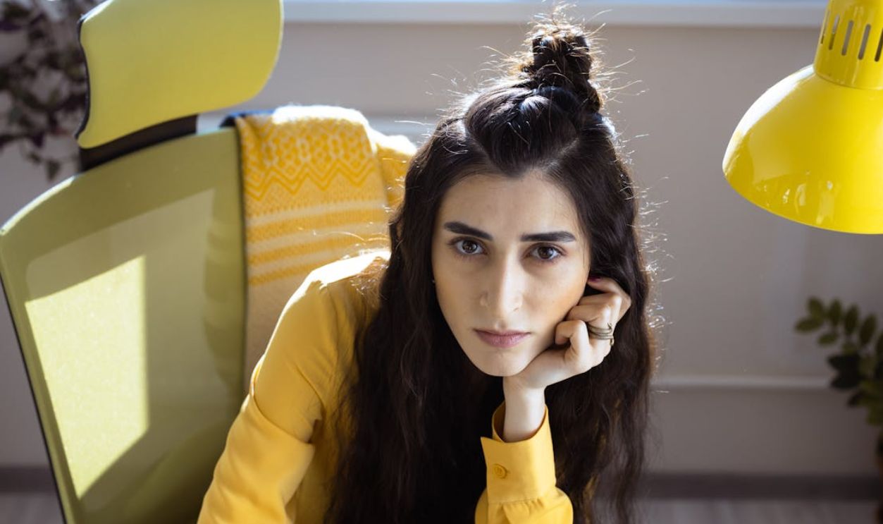 Portrait of a woman in a yellow-themed office, deep in thought with hand on chin