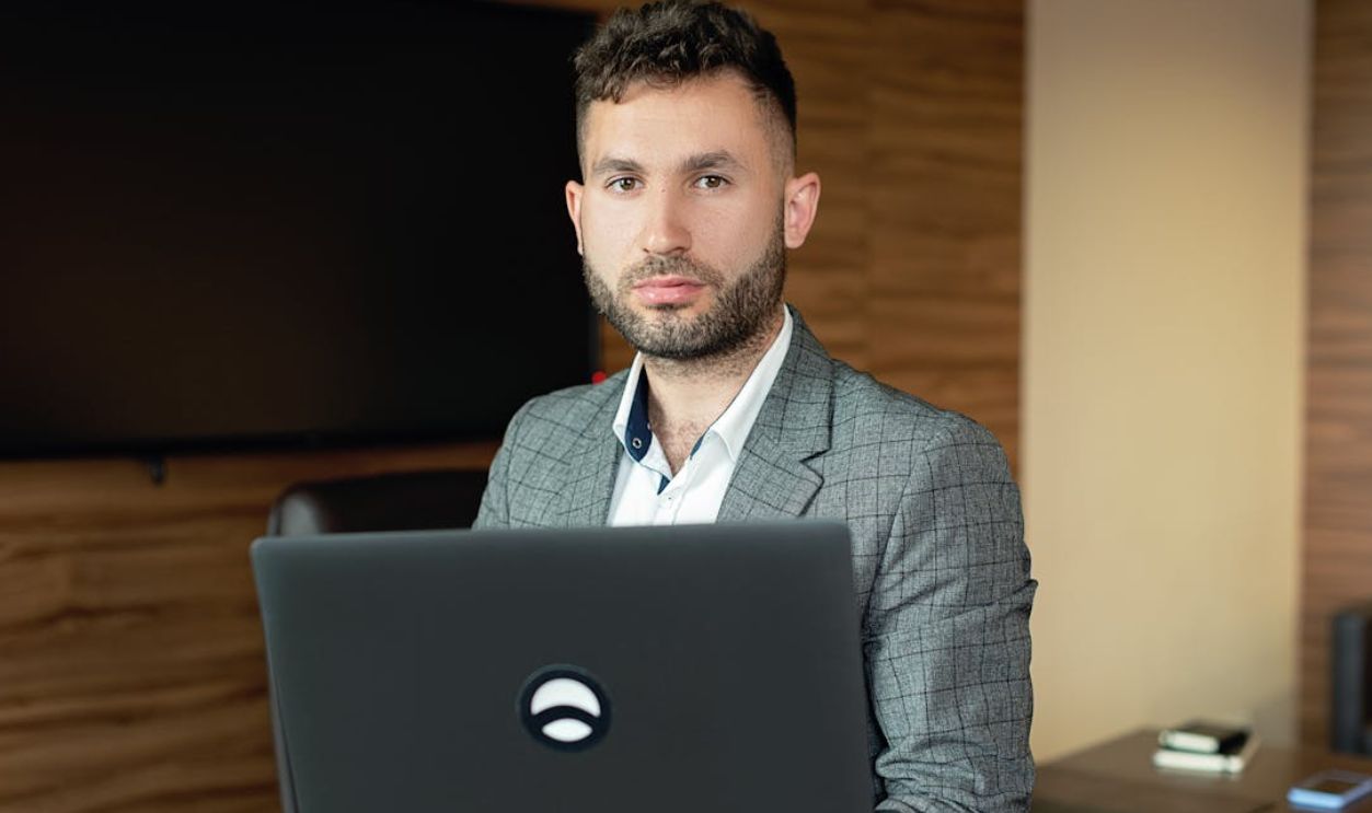 Businessman with facial hair working on a laptop in a modern office setting