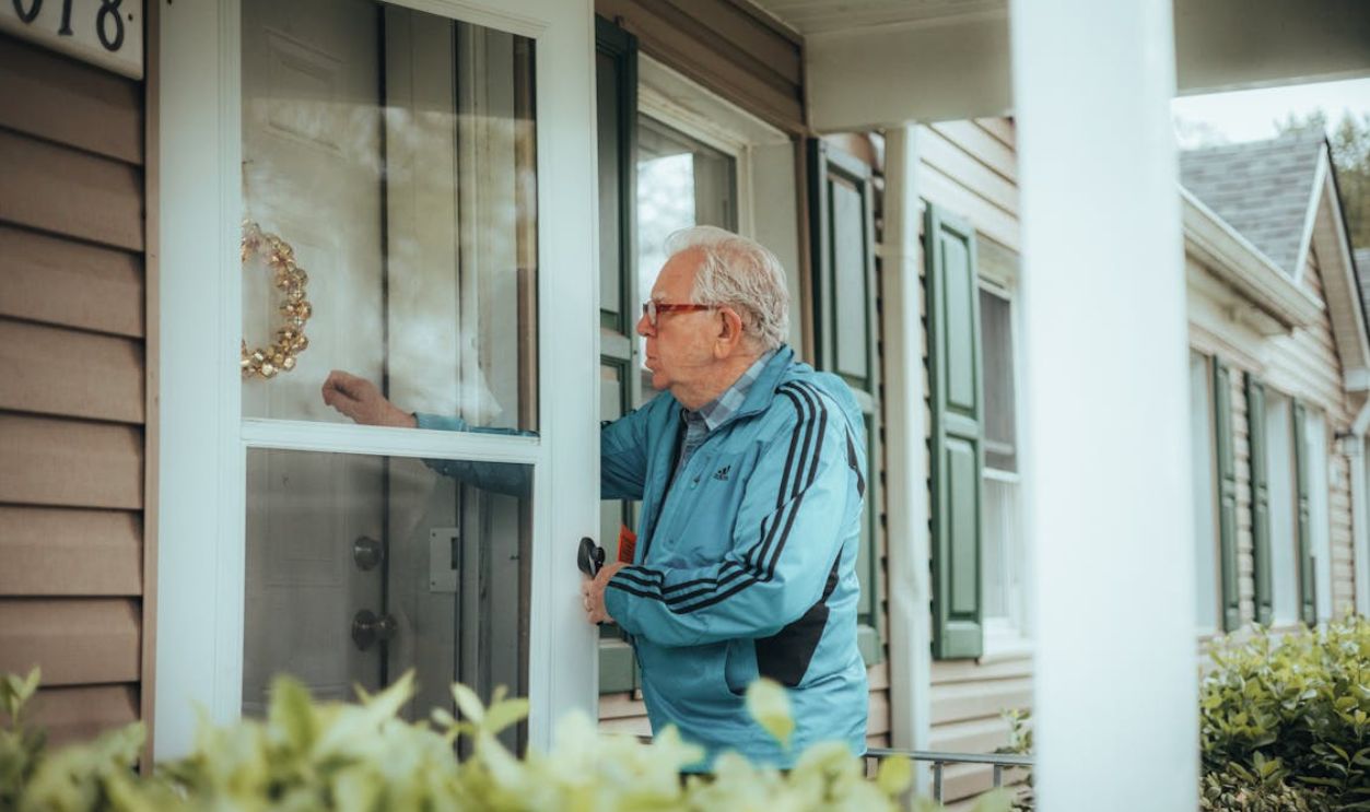 Elderly man in a blue jacket knocking on a suburban house door, showcasing community life.