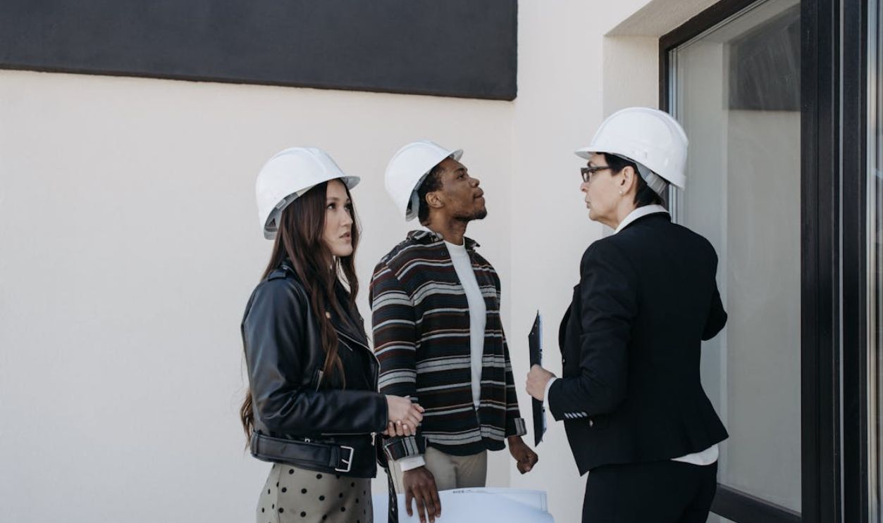 A diverse group of professionals in construction helmets reviewing property plans outdoors.