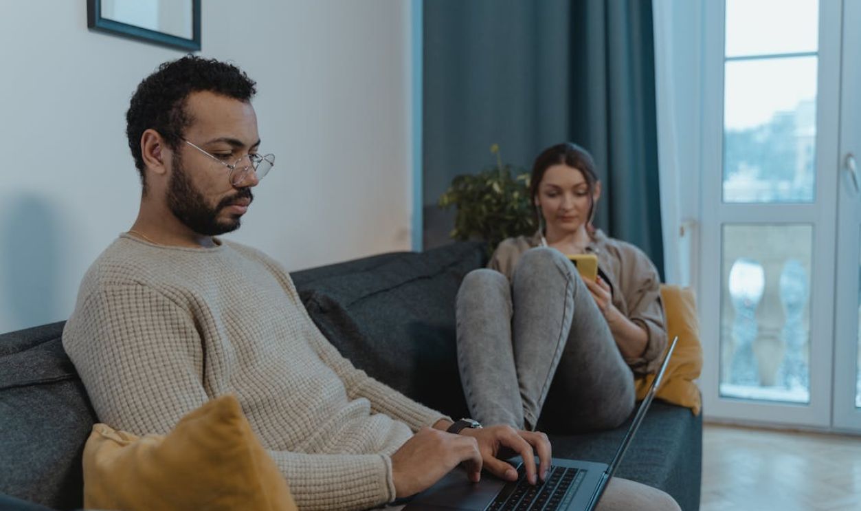 A couple in a cozy living room, each engaged with different tech devices, showcasing modern lifestyle.