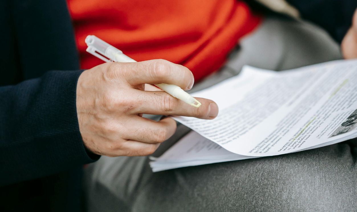 A focused individual reviewing documents outdoors, pen in hand, wearing vibrant clothing.