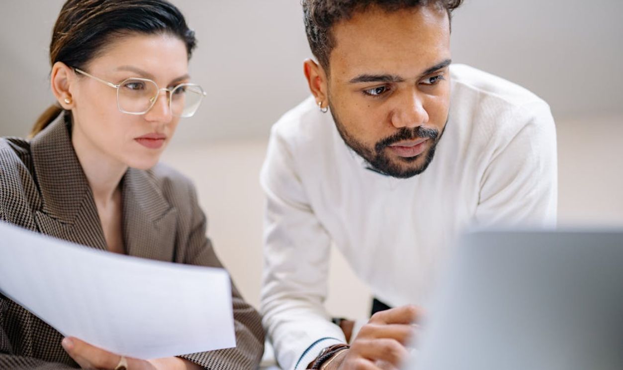 Two colleagues engaged in teamwork, analyzing documents in a modern office environment.