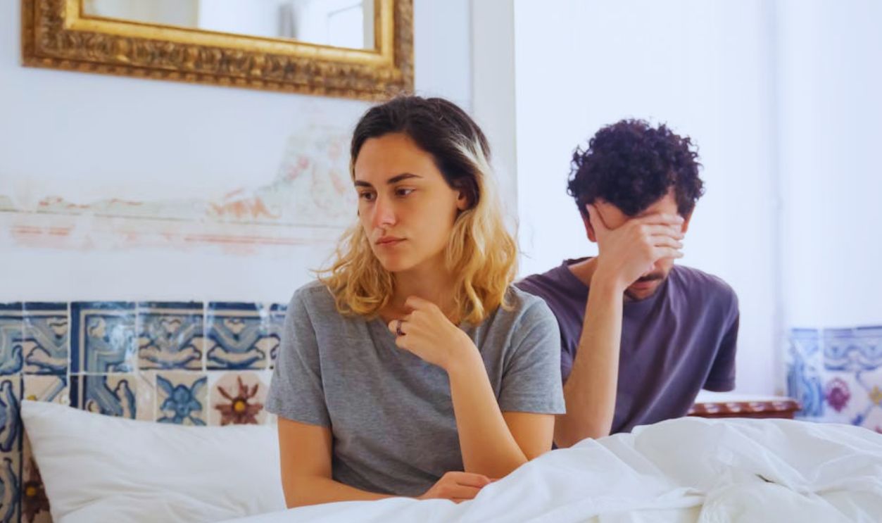 A couple sits together in a bedroom, experiencing a moment of misunderstanding