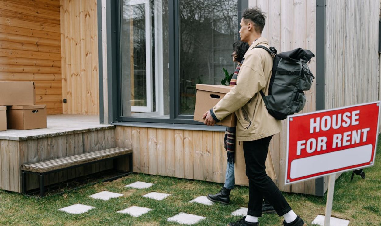 Young couple moving into a new rental home with boxes. Outdoor scene with a rental sign
