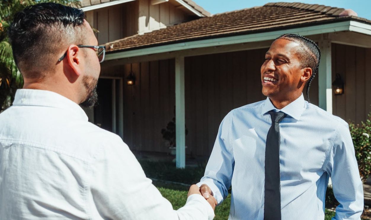 Two real estate professionals shaking hands in front of a new home during a transaction