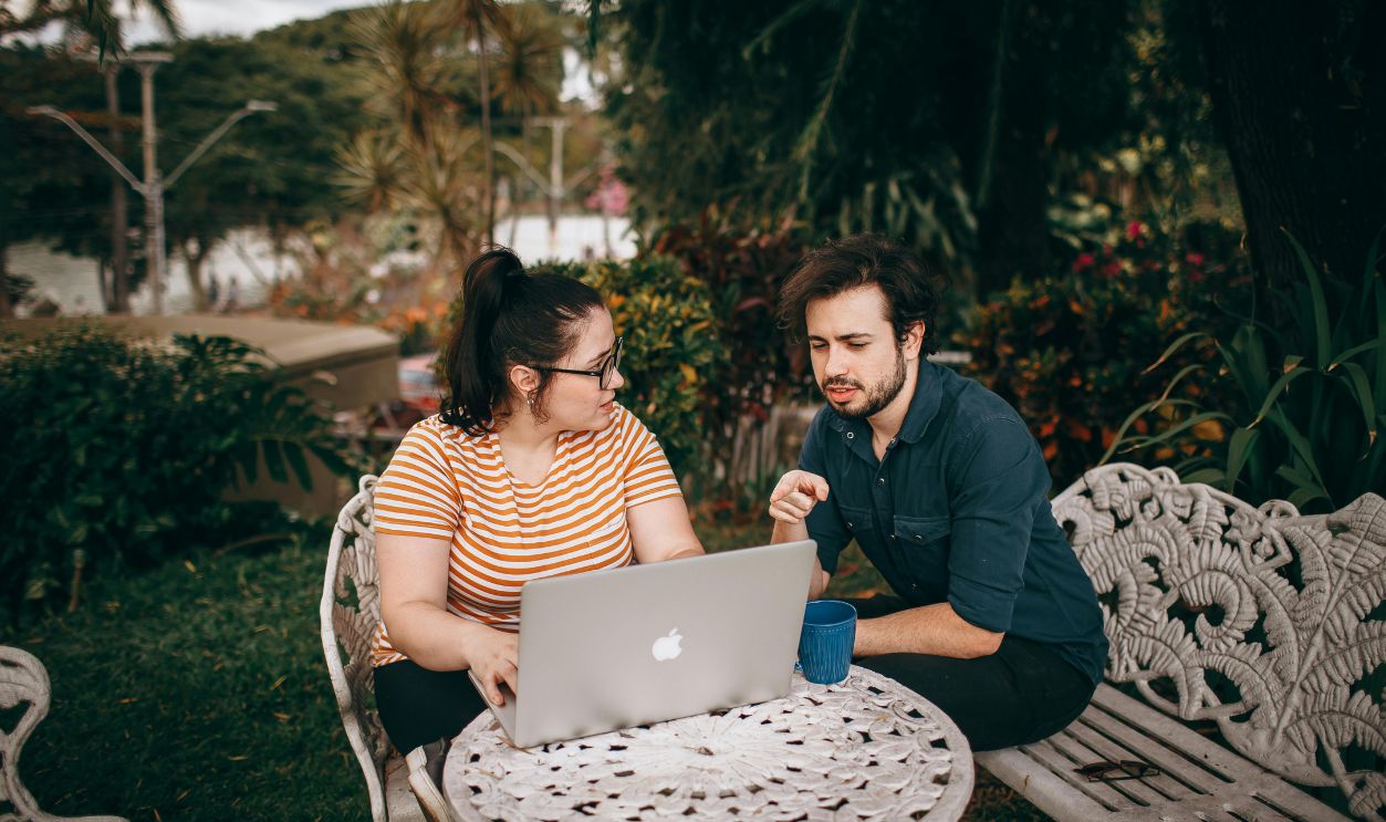 A man and woman working together on a laptop outdoors in a lush garden