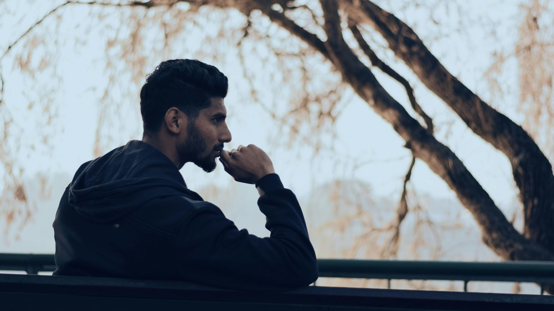 Man in deep thought sitting on a bench in a serene autumn park setting