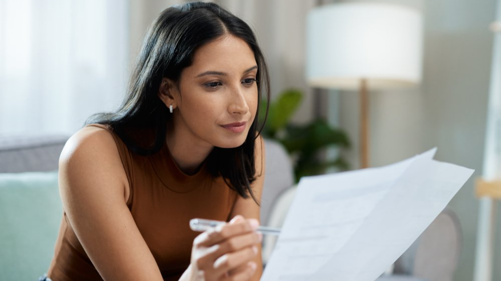 Woman, documents and reading on sofa checking bills