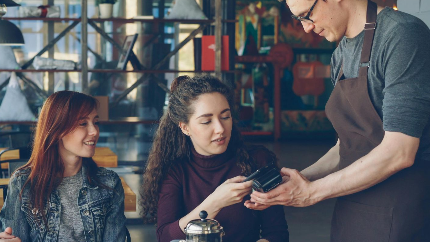Group of friends having coffee and paying with card in a cozy café setting.