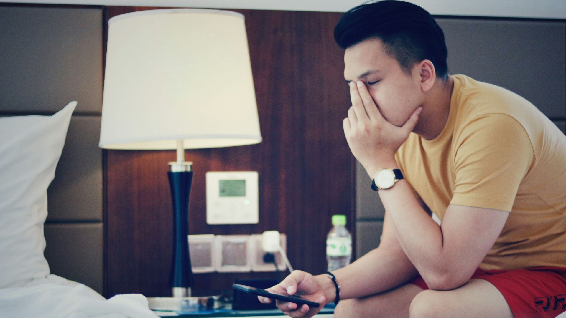 man holding phone and sitting while putting left hand on his face