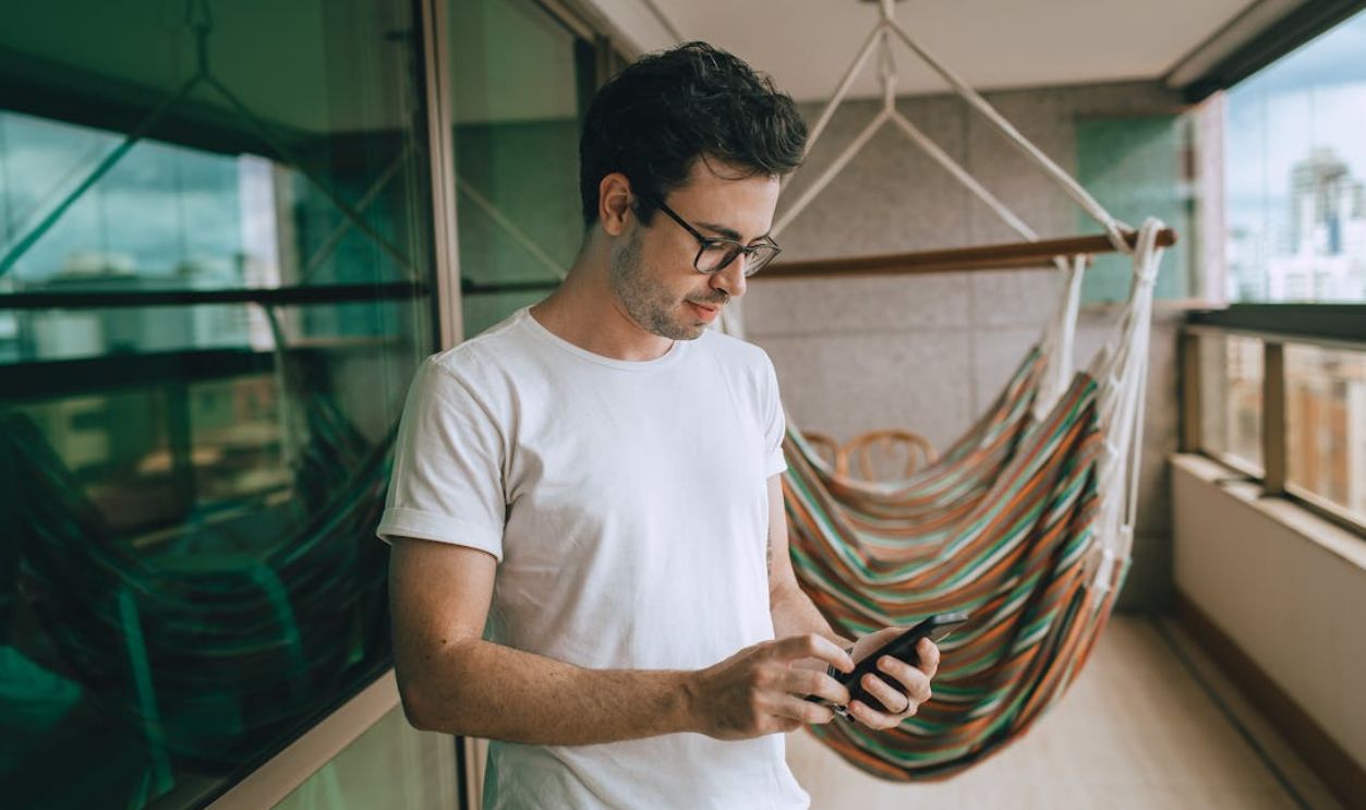 A man using a smartphone on a balcony, reflected in the window behind him