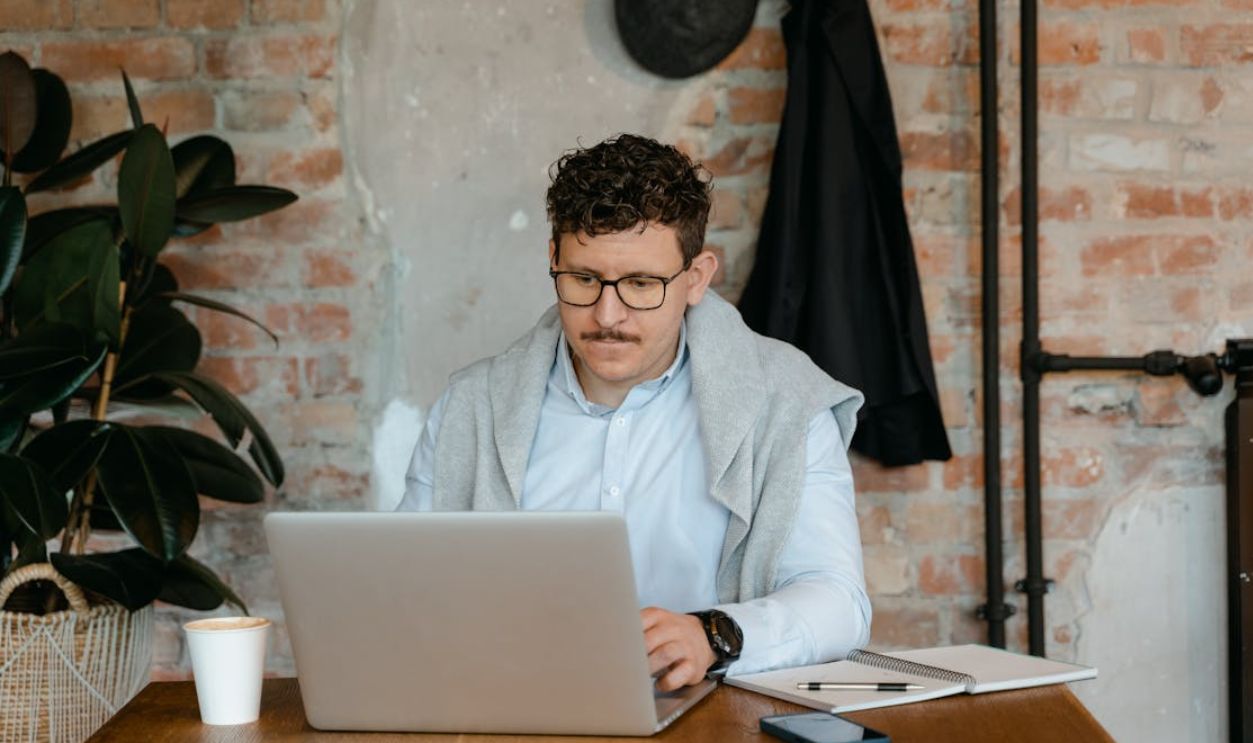 Man with eyeglasses working on a laptop at a wooden table in a rustic office