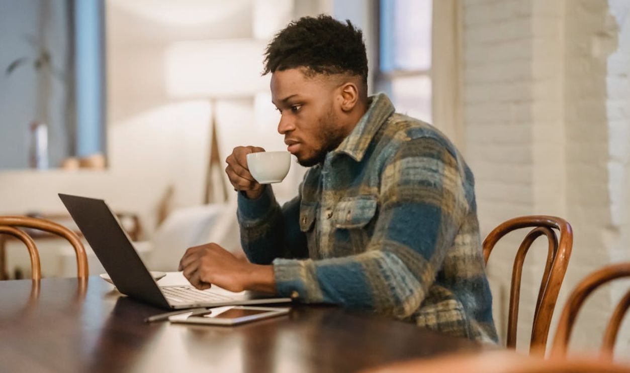 A man attentively works on a laptop while sipping coffee in a cozy home setting