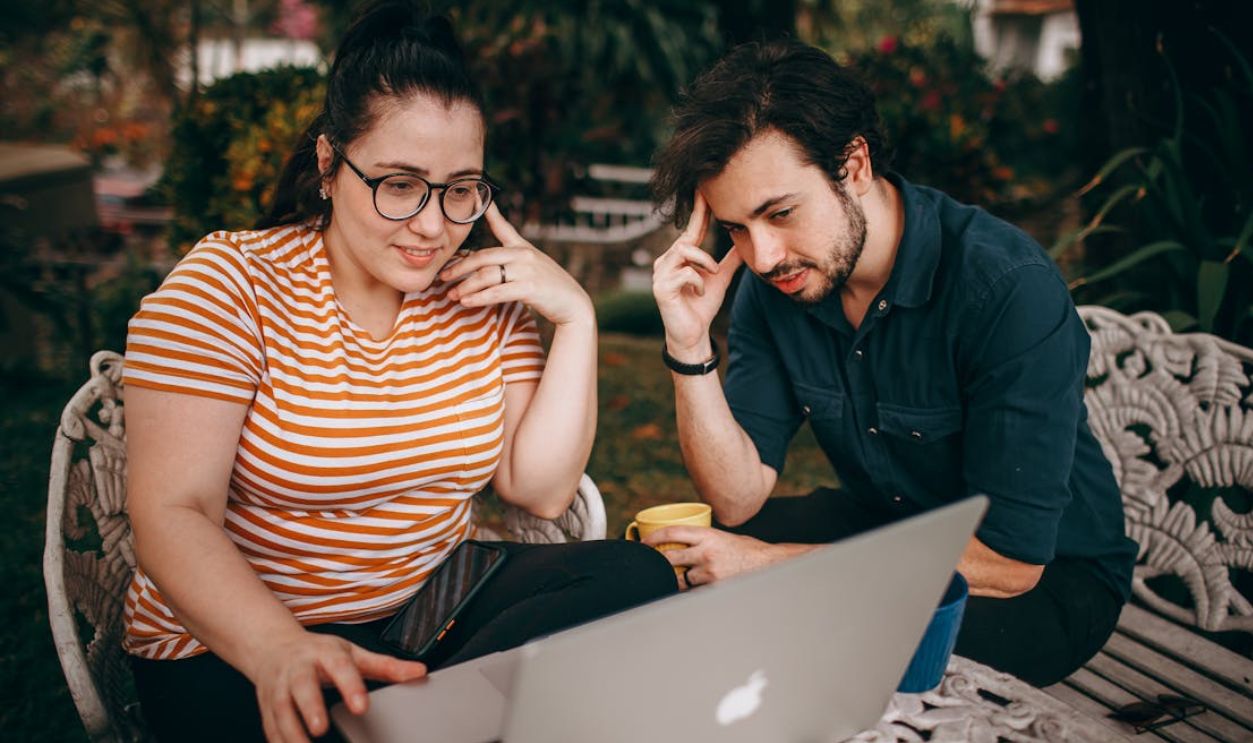 A man and woman working together on a laptop in an outdoor setting, sharing ideas